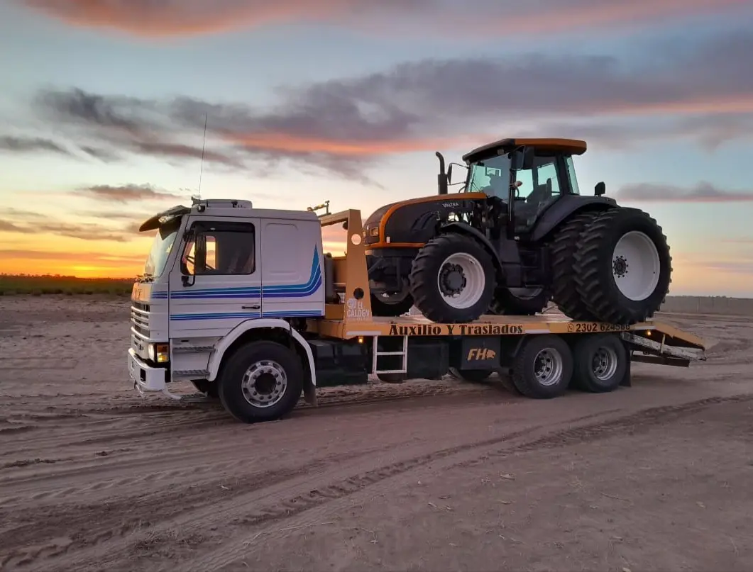 Camión camilla Guinche trasladando un tractor al atardecer